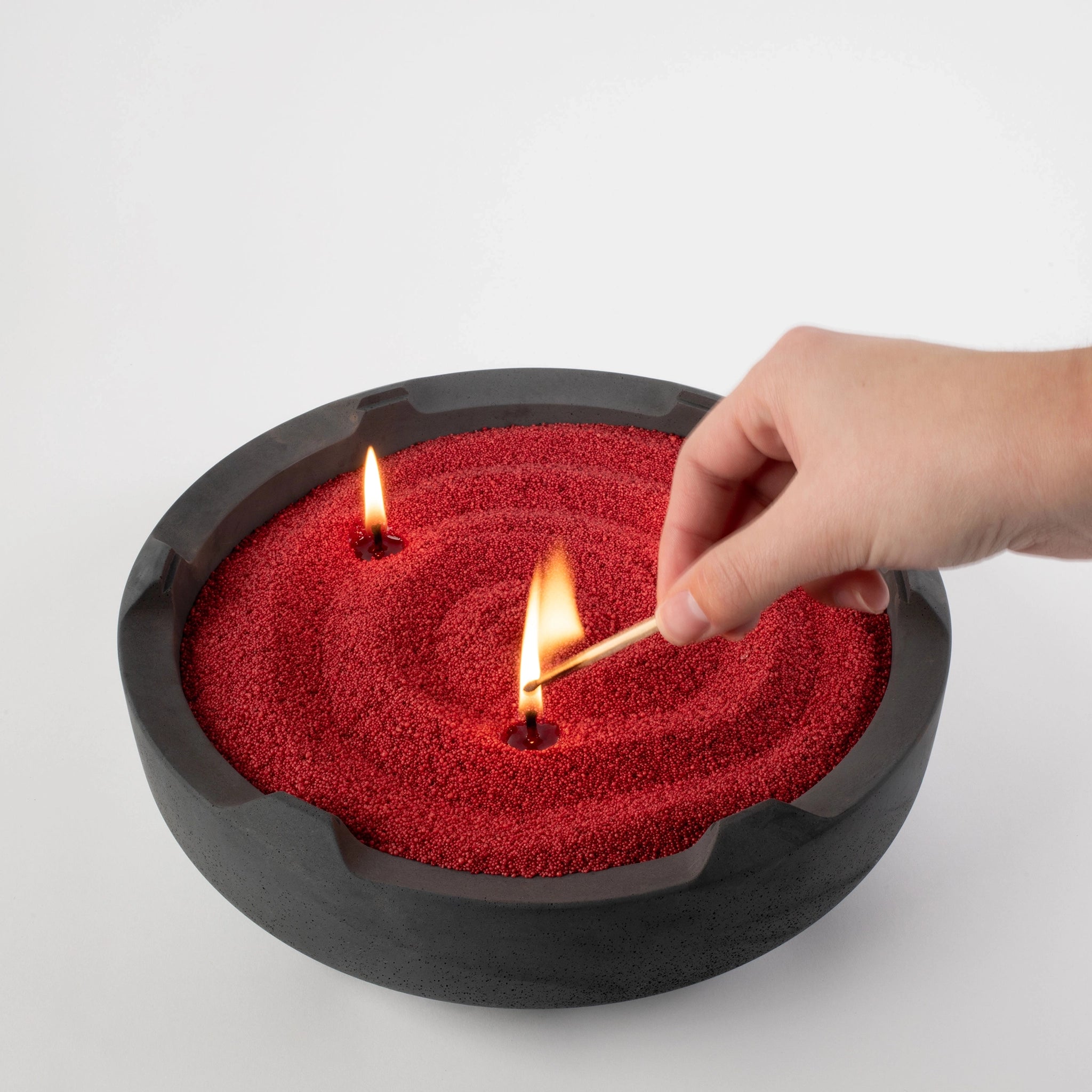 Someone lighting candle wick in Halo Grande concrete base with Crimson Red Sand Wax and white background